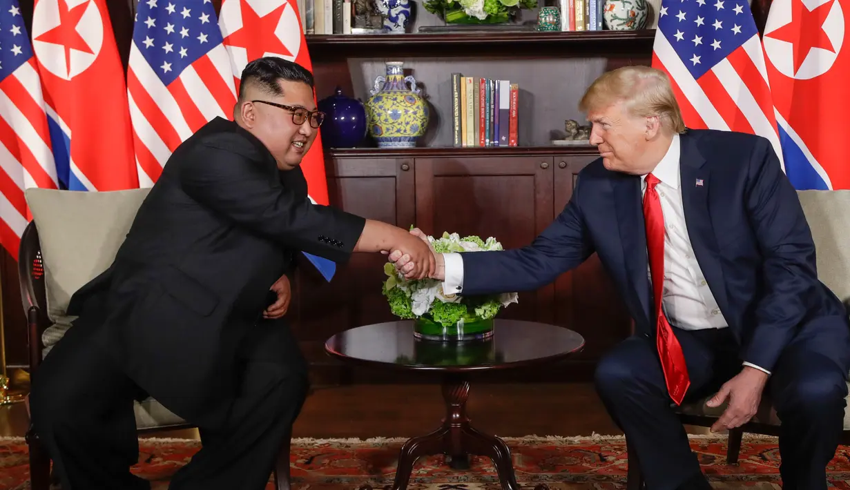 Presiden Amerika Serikat (AS) Donald Trump  dan Pemimpin Korea Utara, Kim Jong-un bersalaman dalam pertemuan bersejarah di resor Capella, Pulau Sentosa, Selasa (12/6). Trump dan Kim menyempatkan diri untuk menyapa jurnalis. (AP/Evan Vucci)