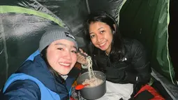 Febby Rastanty tersenyum saat menikmati mie instan bersama temannya yang bernama Bella di dalam tenda selama mendaki Gunung Merbabu dan mengunggah ke akun Instagram miliknya. (Instagram/febyraastanty)