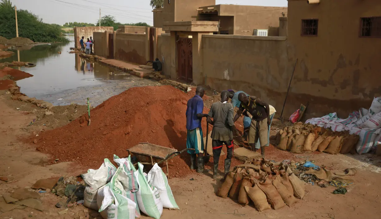 Pria Sudan mengisi karung pasir untuk membuat penghalang banjir di sekitar rumah mereka di area alqamayir di kota kembar ibu kota Omdurman (26/8/2020). (AFP Photo/Ashraf Shazly)