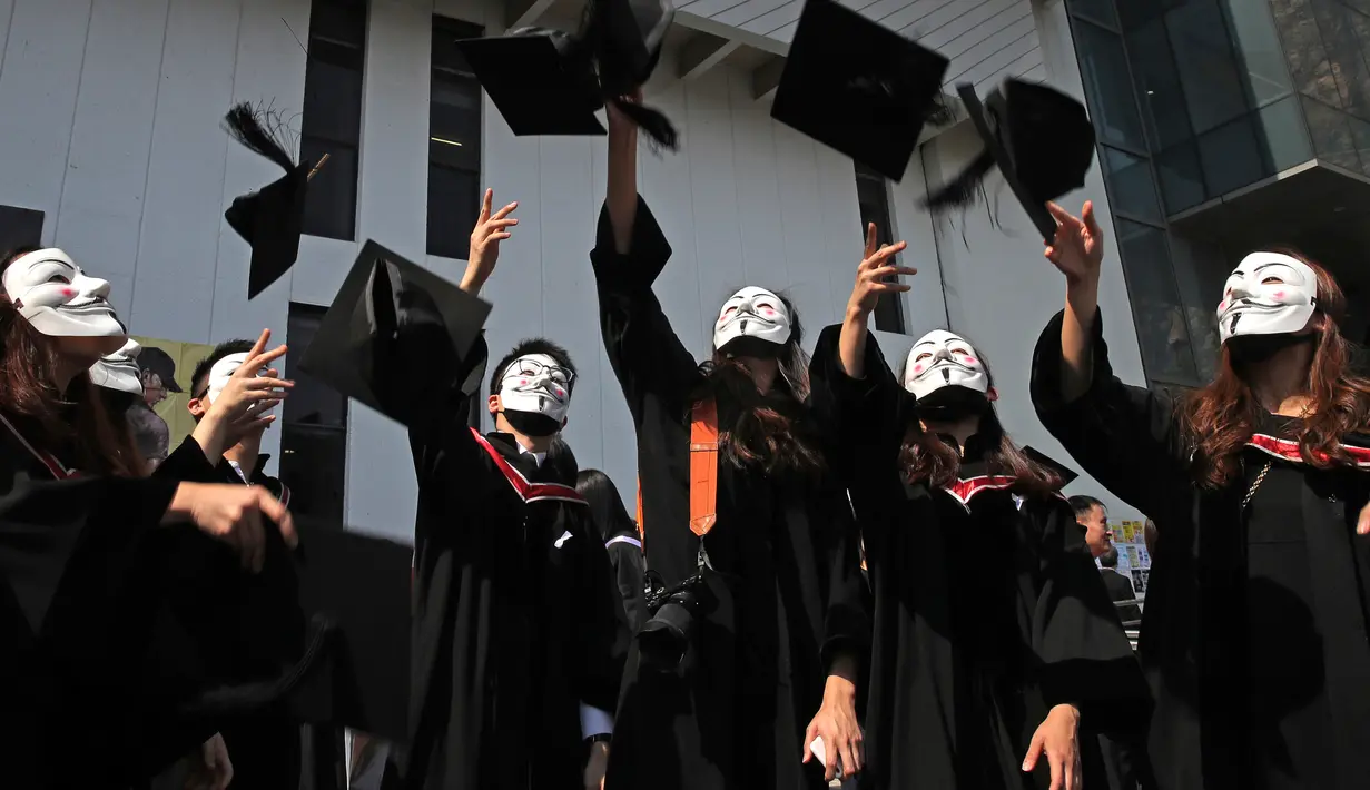 Wisudawan bertopeng Guy Fawkes melemparkan topi wisuda setelah upacara kelulusan mereka di Chinese University of Hong Kong, Hong Kong, Kamis (7/11/2019). Sekitar seribu mahasiswa mengabaikan larangan mengenakan topeng yang dikeluarkan pemerintah pada Oktober 2019. (AP/Kin Cheung)