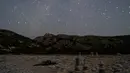 Dalam foto yang diambil dengan kecepatan rana lambat ini memperlihatkan sebuah meteor Perseid memercik saat memasuki atmosfer Bumi ketika seorang pria tidur di Pantai Tripiti, Pulau Gavdos, titik paling selatan Yunani dan Eropa, Minggu (13/8/2023) dini hari. (AP Photo/Petros Giannakouris)