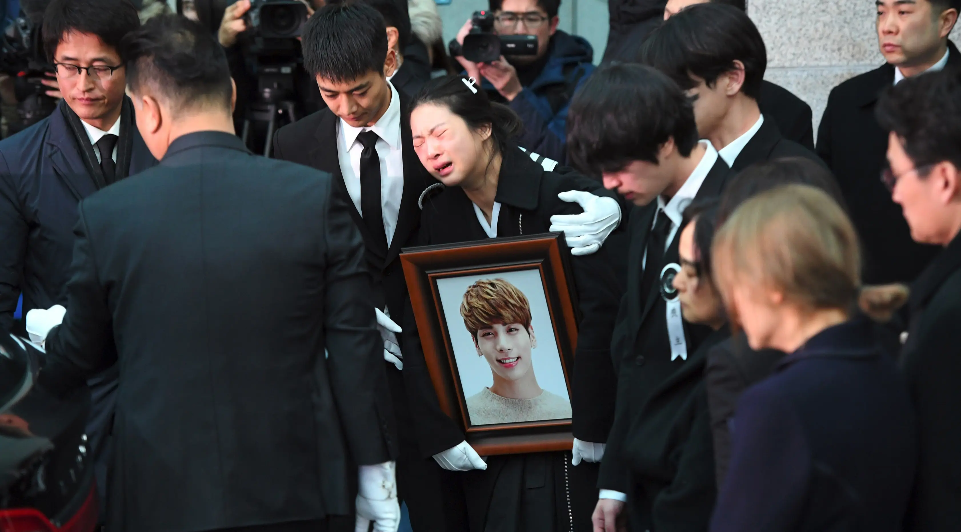Kakak Jonghyun menangis dalam pelukan Minho SHINee saat peti jenazah dimasukkan ke mobil menuju tempat pemakaman dari rumah persemayaman di Asan Hospital, Seoul, Kamis (21/12). Kesedihan menyelimuti pelepasan peti jenazah Jonghyun. (JUNG Yeon-Je/AFP)