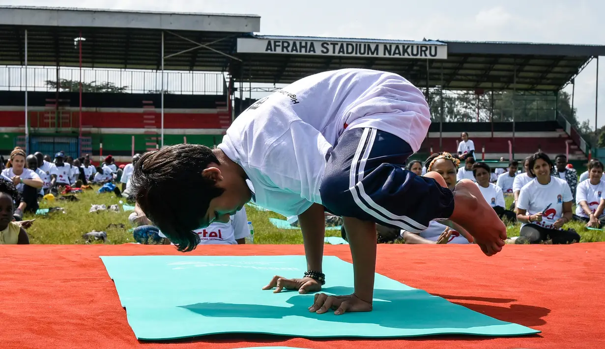 Seorang anak lelaki melakukan gerakan yoga saat mengikuti yoga massal di Stadion Afraha, Nakuru, Kenya (15/6/2019). Hari Yoga Internasional, yang setiap tahun dirayakan pada 21 Juni, pertama kali diusulkan Perdana Menteri India Narendra Modi pada 2014 ke Majelis Umum PBB. (AFP Photo/Suleiman Mbatiah