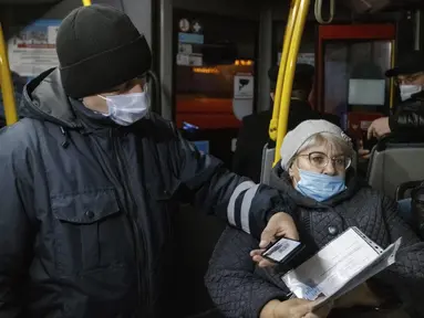 Seorang petugas (kiri) memeriksa kode QR penumpang yang membuktikan tidak adanya infeksi virus corona pada layar ponsel pintar, di dalam bus di Kazan, Senin (22/11/2021). Kazan, menjadi yang pertama di Rusia yang mulai mewajibkan bukti vaksinasi sebelumnya untuk akses transportasi umum. (AP Photo)