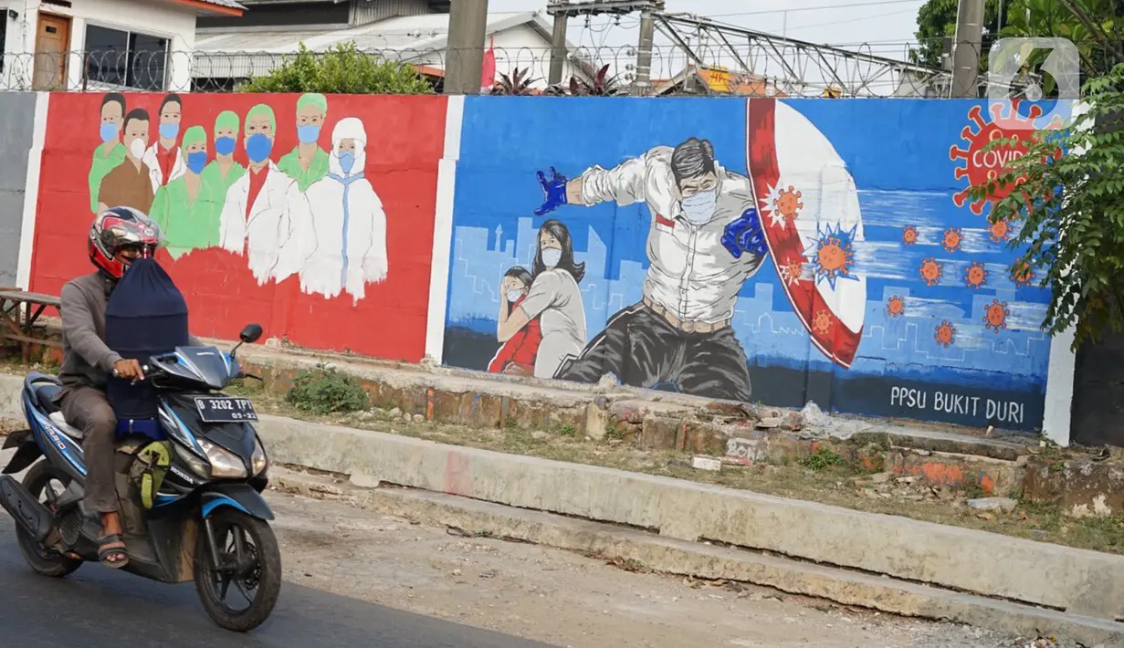 Pengendara motor melintas di depan mural bertema covid-19 di Bukit Duri, Jakarta, Minggu (30/8/2020). Mural yang dibuat petugas PPSU bertujuan mengingatkan masyarakat akan bahaya covid-19, sehubungan dengan masih tingginya jumlah kasus positif covid-19 di Jakarta. (Liputan6.com/Immanuel Antonius)
