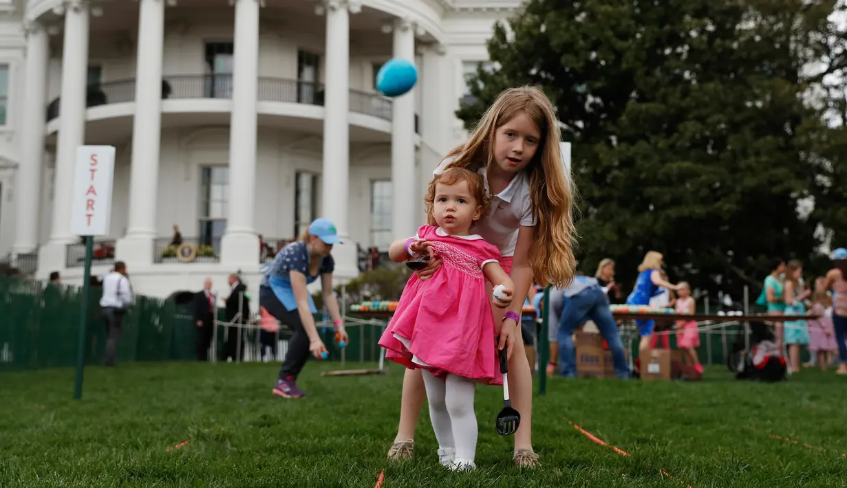 Caroline Earnshaw (10) membantu adiknya menggelindingkan telur saat lomba perayaan Paskah di halaman Gedung Putih, Washington, Senin (17/4). Lomba yang digelar setiap tahun ini merupakan lomba menggelindingkan telur yang ke-139. (AP Photo/Carolyn Kaster)
