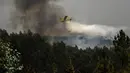 Sebuah pesawat pemadam kebakaran menjatuhkan air ke area kebakaran di Amendoa, Macao, di Portugal tengah (21/7/2019). Lebih dari seribu petugas pemadam kebakaran berjuang untuk memadamkan kebakaran hutan tersebut. (AFP Photo/Patricia De Melo Moreira)