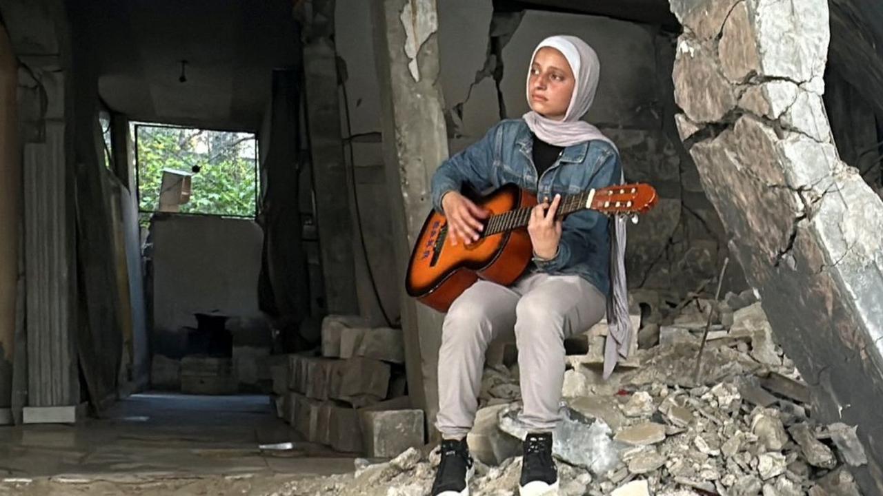 Seorang mahasiswi kedokteran Palestina, Rahaf Nasser memainkan musik di antara reruntuhan untuk menghibur anak-anak di Deir Al-Balah, Jalur Gaza, pada 5 Juni 2024. Tidak dapat melanjutkan studi kedokterannya karena peperangan, Rahaf Nasser menghabiskan ha