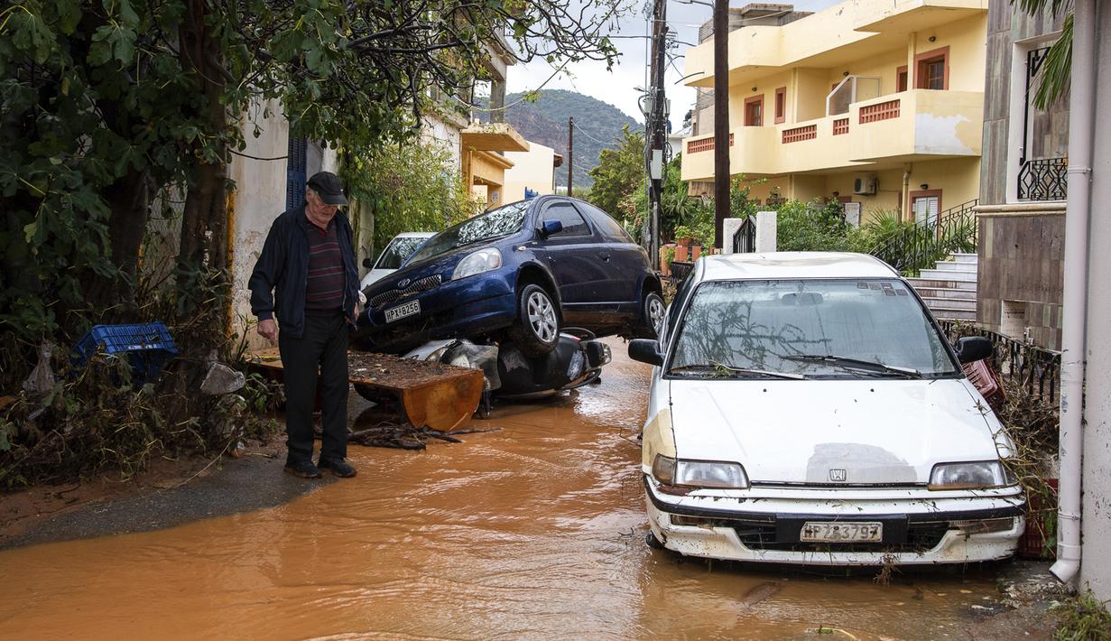 Mobil-mobil menumpuk saat warga menyeberang jalan melalui air banjir setelah hujan lebat di desa Malia, pulau Kreta, Yunani, Selasa (10/11/2020). Banjir merusak jalan, membanjiri ratusan rumah, dan menyeret mobil ke laut di tengah hujan deras yang sedang berlangsung. (AP Photo/Harry Nakos)
