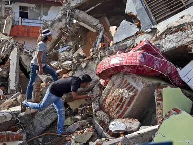 Warga memeriksa bangunan yang runtuh akibat gempa di Mamuju, Sulawesi Barat, Indonesia, Senin (18/1/2021). Hingga Minggu 17 Januari 2021 pukul 20.00 WIB, BNPB melaporkan jumlah korban meninggal akibat gempa Sulawesi Barat menjadi 81 orang. (AP Photo/Yusuf Wahil)