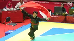 Pesilat Indonesia, Komang Harik Adi Putra mengibarkan bendera Merah Putih usai mengalahkan pesilat Malaysia Mohd Al Jufferi Jamari dalam babak final Kelas E Putra Asian Games 2018 di TMII, Jakarta, Senin (27/8). (Merdeka.com/Arie Basuki)