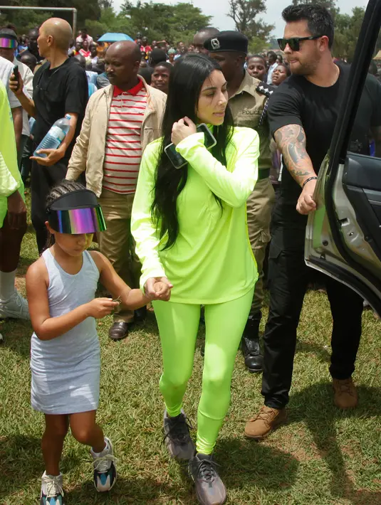 Kim Kardashian dan sang putri, North West menuju sebuah kendaraan setelah bersama suaminya, Kanye West mengunjungi Kampung Anak UWESCO di Masulita, Uganda, Selasa (16/10). UWESO merupakan desa untuk menampung anak-anak yatim piatu. (AP/Stephen Wandera)