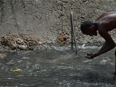 Seorang pria mengeluarkan lumpur dari dasar saluran pembuangan saat dia mencari logam berharga di Sungai Guaire, di Caracas, Venezuela (1/2). Puluhan warga mencari logam atau tembaga setiap hari di Sungai Guaire. (AFP Photo/Federico Parra)
