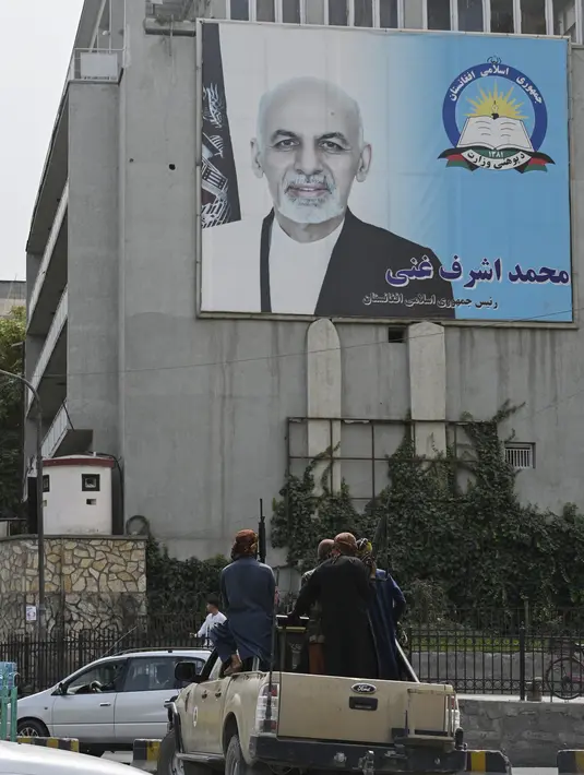 Pejuang Taliban berpatroli melewati poster Presiden Afghanistan Ashraf Ghani yang digulingkan di Kabul (17/8/2021). Taliban bergerak untuk segera memulai kembali ibu kota Afghanistan setelah pengambilalihan Kabul n dan menyuruh staf pemerintah untuk kembali bekerja. (AFP/Wakil Kohsar)