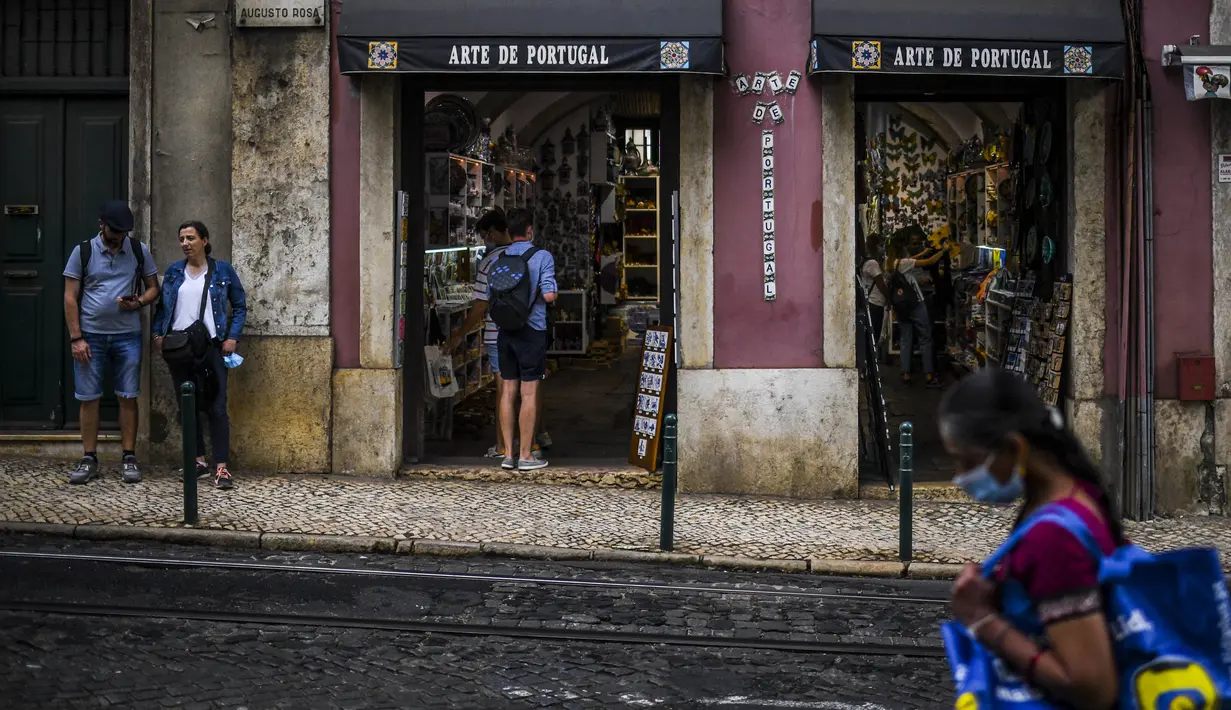 Turis berdiri di luar toko suvenir di pusat kota Lisbon, Portugal, Senin (13/9/2021). Portugal hari ini mengakhiri aturan wajib penggunaan masker di jalan-jalan. (PATRICIA DE MELO MOREIRA / AFP)