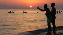 Pengunjung berenang sambil menikmati pemandangan matahari terbenam di Pantai Santa Maria Del Focalo, Pulau Sisilia, Italia, 7 Agustus 2017. Pantai Santa Maria Del Focalo menjadi salah satu tujuan objek wisata favorit di Italia. (ludovic MARIN/AFP)
