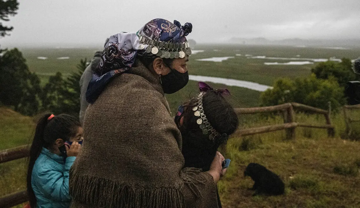 Seorang nenek Adat Mapuche memeluk cucunya saat gerhana matahari total di Carahue, La Araucania, Chile, Senin (14/12/2020). Gerhana matahari total terlihat dari Chile dan wilayah Patagonia utara Argentina. (AP Photo/Esteban Felix)