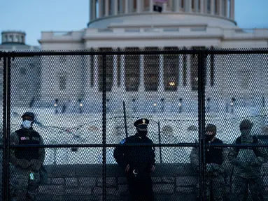 Petugas Kepolisian Capitol berjaga bersama pasukan Garda Nasional di belakang pagar pengendali kerumunan di sekitar Capitol Hill AS di Washington, Kamis (7/1/2021). Peristiwa penyerbuan di gedung Capitol Hill AS dilakukan oleh massa pendukung Donald Trump pada 6 Januari. (Brendan Smialowski/AFP)