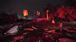 Warga yang diterangi oleh lampu truk pemadam kebakaran berdiri di antara puing-puing setelah tornado menyapu daerah di Arabi, La., Selasa (22/3/2022). Tornado menerjang bagian New Orleans dan sekitarnya Selasa malam, menghancurkan kabel listrik dan menyebarkan puing-puing di bagian kota. (AP Photo/G