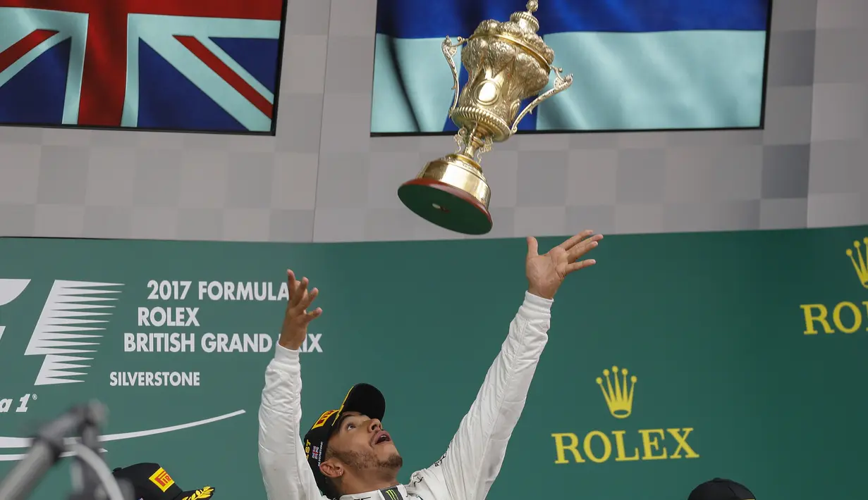 Pebalap Mercedes, Lewis Hamilton, melempar trofi usai menjuarai F1 GP Inggris di Sirkuit Silverstone, Minggu (16/7/2017). Pebalap 32 tahun asal Inggris itu melahap 51 lap dengan catatan waktu 1 jam 21 menit 27,430 detik. (EPA/Valdrin Xhemaj)