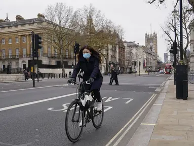 Seorang wanita mengenakan masker saat dia bersepeda di Westminster, di London, Kamis (16/12/2021). Inggris mencatat jumlah tertinggi infeksi COVID-19 baru yang dikonfirmasi pada hari Rabu (15/12) sejak pandemi dimulai. (AP Photo/Alberto Pezzali)