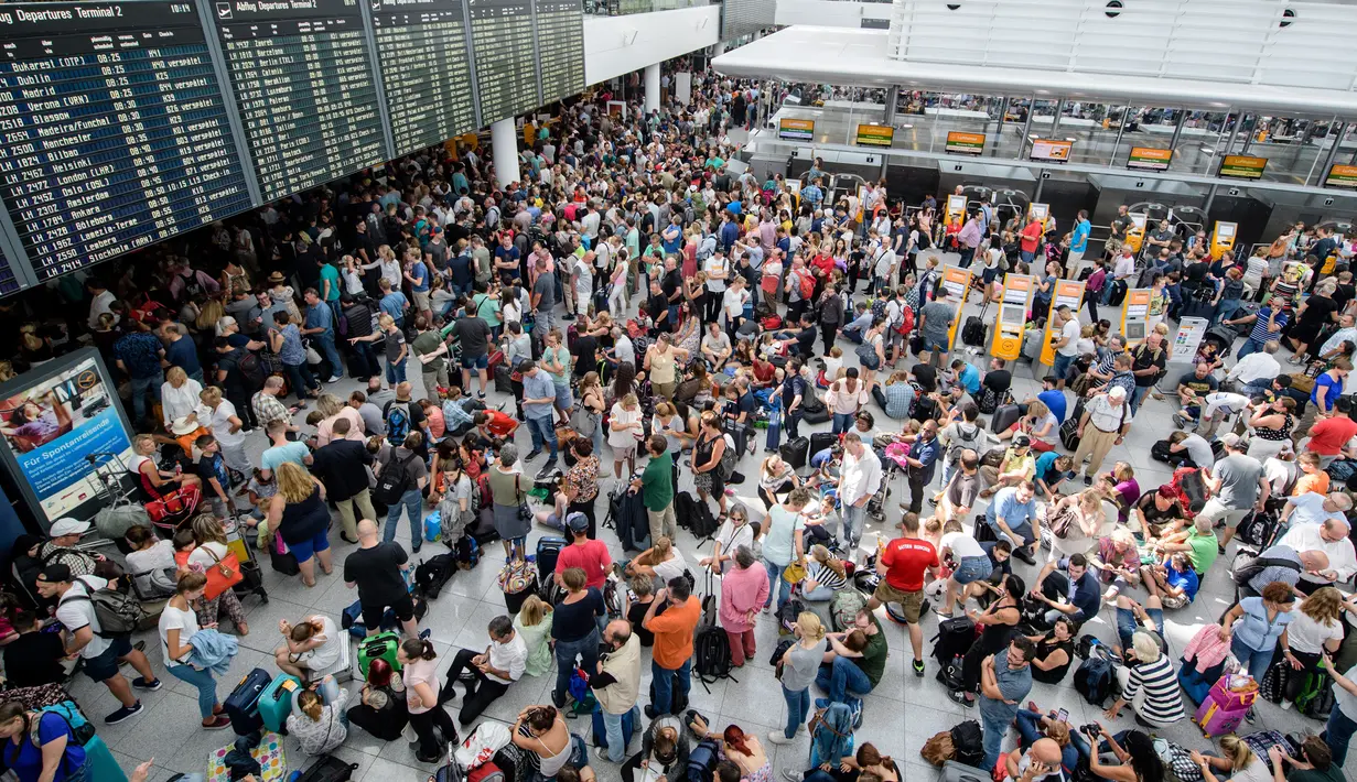 Calon penumpang berkumpul di depan papan jadwal penerbangan di Terminal 2 Bandara Munich, Sabtu (28/7). Kepolisian Jerman menutup terminal 2 bandara tersebut setelah seorang wanita dilaporkan menyusup melewati pos pemeriksaan. (MATTHIAS BALK /DPA/AFP)