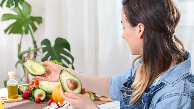 Seorang perempuan memegang sebuah alpukat di meja makan (Foto Dok: Freepik/pvproductions)