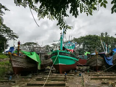 Para pekerja berjalan melewati kapal-kapal yang sedang diperbaiki di galangan kapal di tepi Sungai Yangon, yang terletak di pinggiran Yangon, Myanmar (30/7/2019). (AFP Phot/Sai Aung Main)