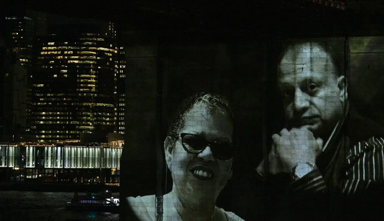 Gambar korban diproyeksikan pada Jembatan Brooklyn saat Hari Peringatan COVID-19 di Brooklyn, New York, Amerika Serikat, 14 Maret 2021. Foto hitam putih besar yang menunjukkan para korban ditampilkan di Jembatan Brooklyn. (Kena Betancur/AFP)