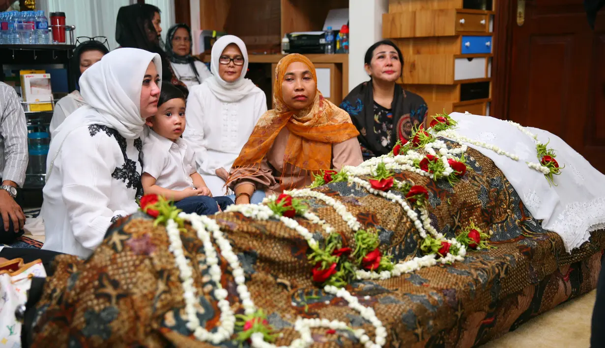 Pandangan kosong sang istri dengan baju dan jilbab putih yang memangku seorang anak kecil yang berada di sebelah jenazah suaminya, Sys Ns yang meninggal usia 61 tahun. (Nurwahyunan/Bintang.com)