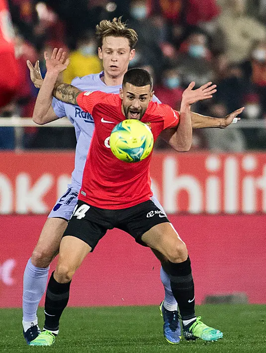 Gelandang Real Mallorca Daniel Rodriguez (depan) berebut bola dengan gelandang Barcelona Frenkie De Jong pada jornada ke-19 Liga Spanyol di Visit Mallorca Estadi, Senin (3/1/2022) dini hari WIB. Barcelona menang 1-0 berkat gol tunggal Luuk de Jong. (JAIME REINA / AFP)