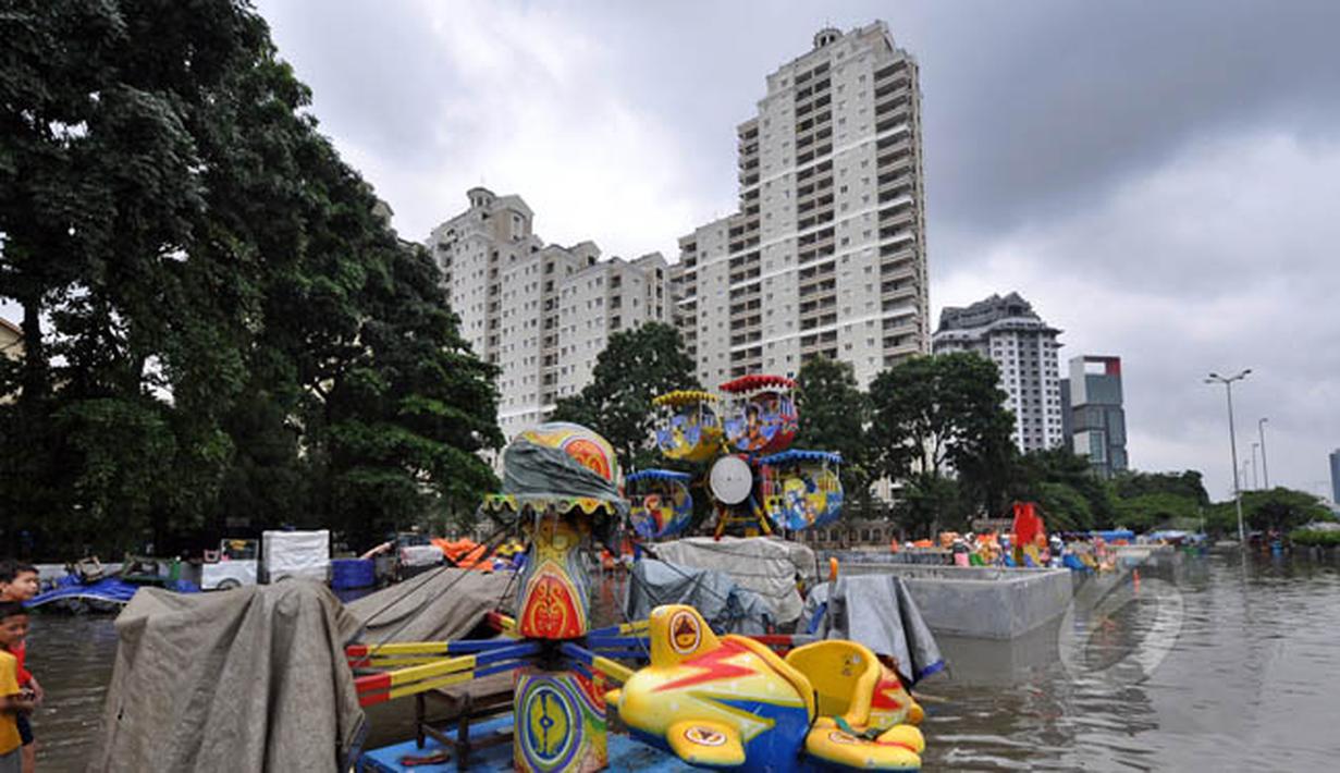 Sejumlah anak bermain di lahan bermain Kemayoran yang terendam banjir, Jakarta, Selasa (10/2). Tingginya curah hujan di wilayah Jakarta mengakibatkan sejumlah fasilitas umum ikut terendam banjir. (Liputan6.com/Faizal Fanani)