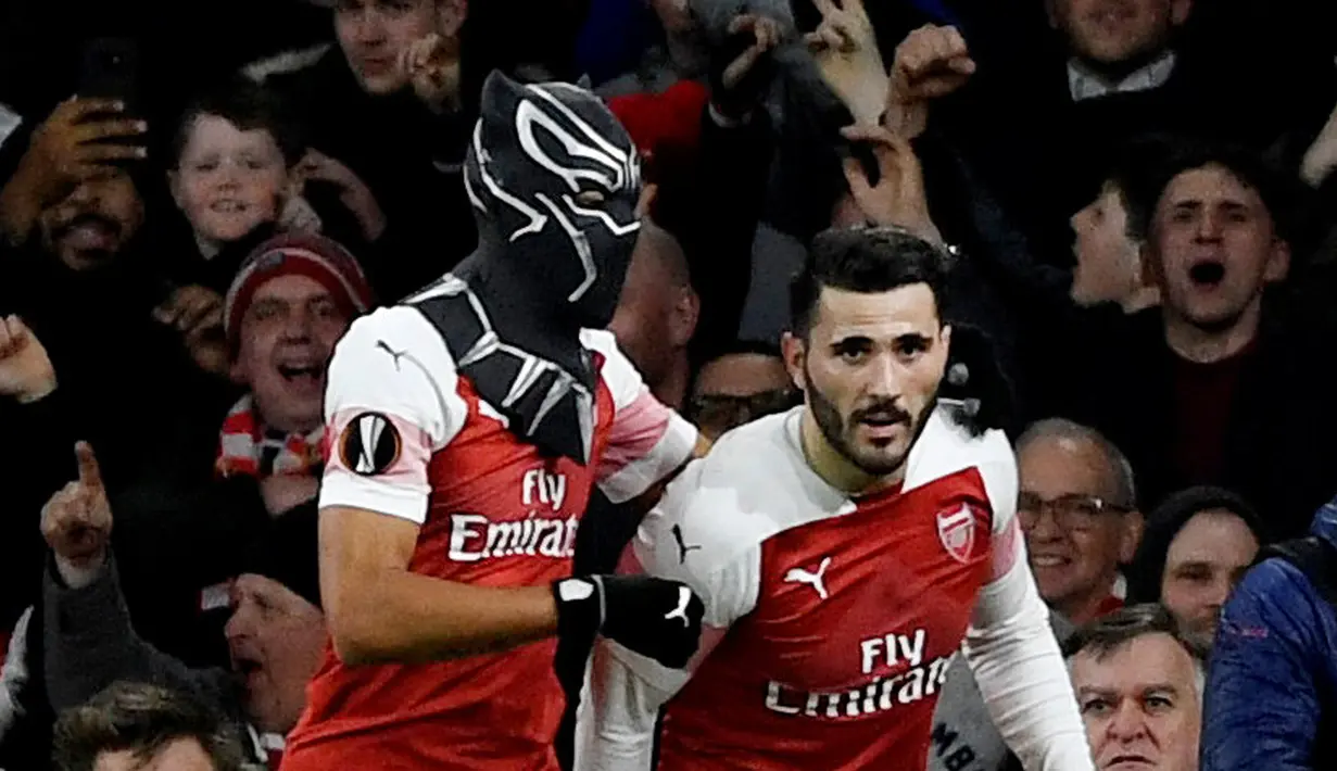 Striker Arsenal Pierre-Emerick Aubameyang (kiri) mengenakan topeng superhero Black Panther usai mencetak gol ke gawang Stade Rennes pada leg kedua babak 16 besar Liga Europa di Stadion Emirates, London, Inggris  (14/3). (Reuters/Tony O'Brien)
