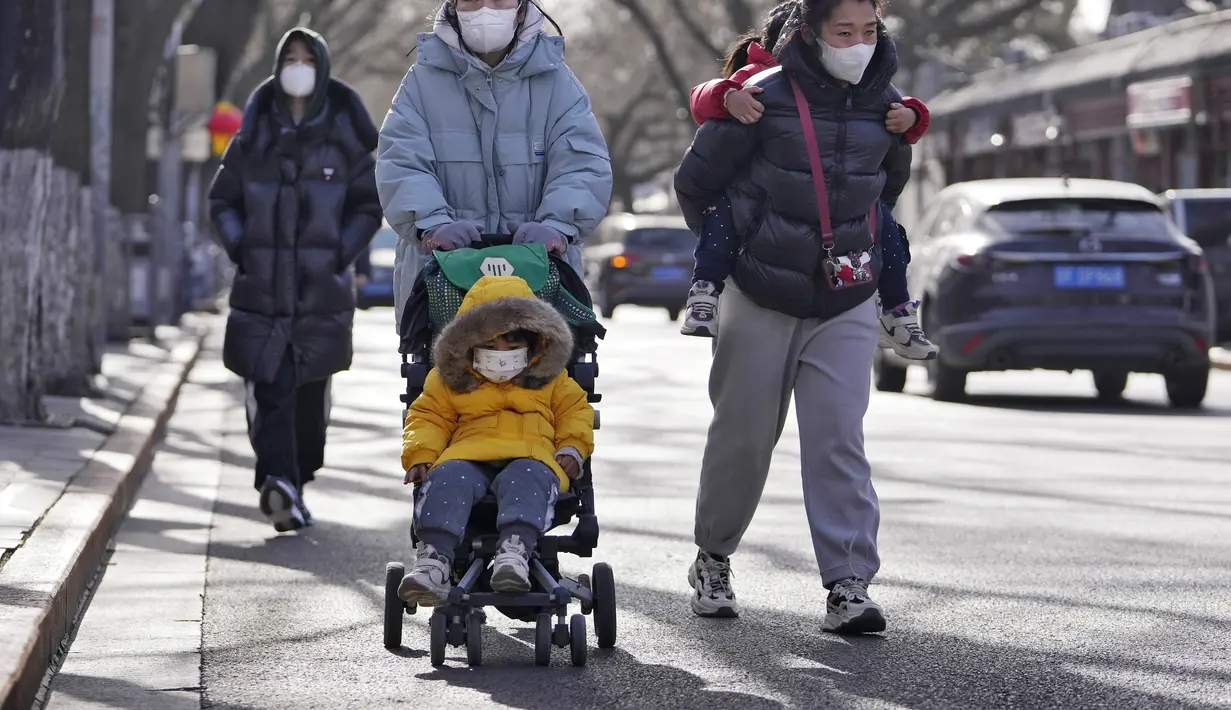 Wanita yang mengenakan masker berjalan dengan anak-anak mereka di jalan menuju Kota Terlarang di Beijing, Selasa (17/1/2023). Penurunan  populasi tersebut lebih dari tiga kali lipat prediksi penurunan sebelumnya pada 2019.
(AP Photo/Andy Wong)