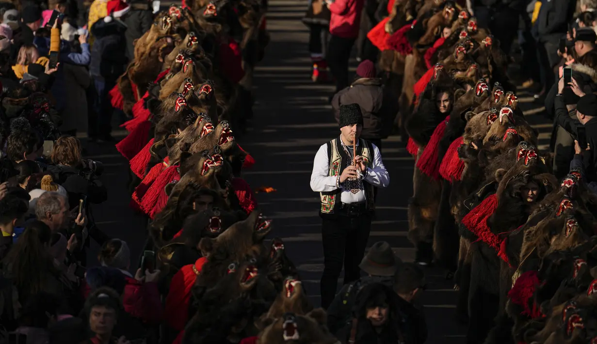 Orang-orang yang mengenakan kostum bulu beruang mengikuti parade di Comanesti, Romania, Jumat, 30 Desember 2022. Dalam tradisi pedesaan pra-Kristen, para penari yang mengenakan kostum berwarna atau kostum bulu binatang pergi dari satu rumah ke rumah lain di desa-desa, bernyanyi dan menari untuk mengusir kejahatan. (AP Photo/Vadim Ghirda)