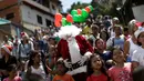 Santa Claus berjalan bersama kerumunan anak-anak di kawasan kumuh Petare di Caracas, Venezuela (11/12). Petare adalah sebuah kawasan yang masuk dalam ibukota Caracas dan terkenal kumuh. (Reuters/Ueslei Marcelino)