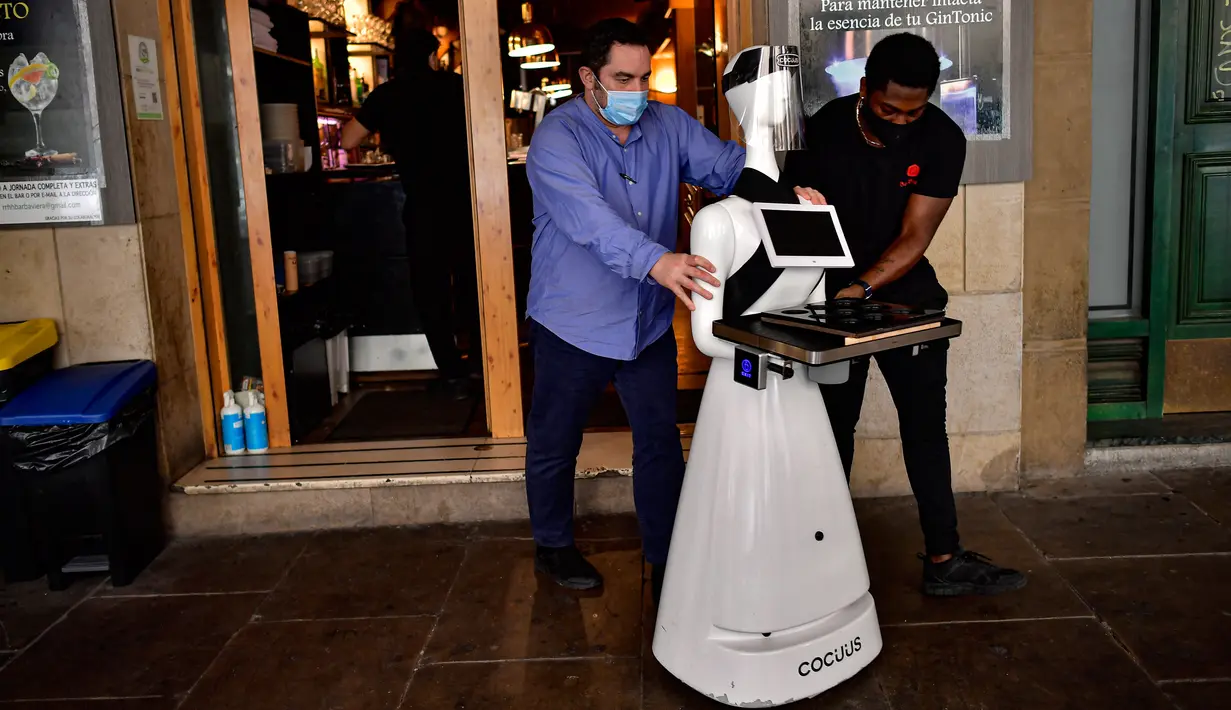 Santo Munoz (kiri) menggerakkan robot yang dikenal sebagai "Alexia" untuk melayani pengunjung sebuah bar di alun-alun Plaza del Castillo, di Pamplona, Spanyol pada 5 Juni 2020. Robot tersebut digunakan untuk mengurangi penyebaran virus corona Covid-19. (AP Photo/Alvaro Barrientos)