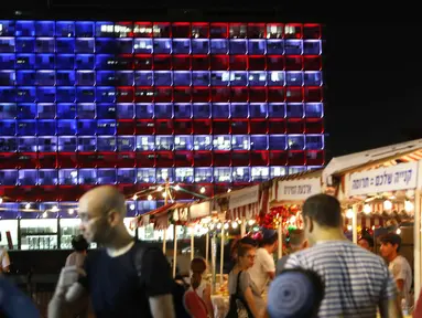 Warga melintas di dekat balai kota Tel Aviv yang dihiasi warna bendera AS untuk menghormati korban penembakan brutal di Las Vegas di Rabin Square, Tel Aviv (2/10). Pelaku penembakan diketahui bernama Stephen Paddock 64 tahun. (AFP Photo/Jack Guez)