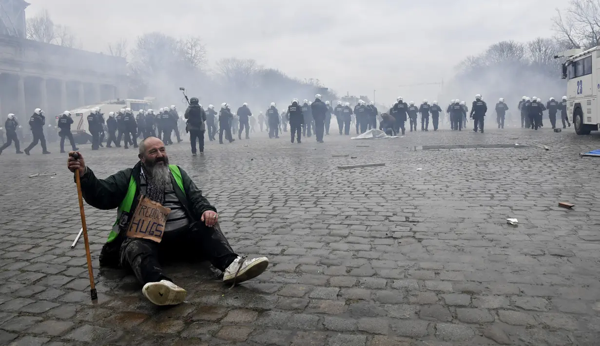 Seorang pria duduk di trotoar saat polisi menghadapi pengunjuk rasa yang menentang tindakan COVID-19 di Brussel, Minggu (23/1/2022). Pengunjuk rasa juga mengkritik kebijakan wajib vaksin untuk beraktivitas di tempat umum maupun mengikuti kegiatan tertentu. (AP Photo/Geert Vanden Wijngaert)