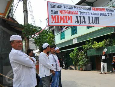 Sejumlah warga berdiri di bawah spanduk penolakan penggusuran Kampung Luar Batang, Penjaringan, Jakarta, Rabu (20/4). Mereka menolak pembongkaran tahap dua yang akan dilakukan Pemprov DKI pada Mei nanti. (Liputan6.com/Yoppy Renato)