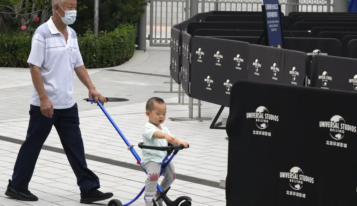 Seorang pria tua mendorong seorang anak di dekat barikade di luar taman hiburan Universal Studios selama uji coba di Beijing (31/8/2021). Universal Studios mengumumkan Senin, 30 Agustus 2021, bahwa taman hiburan pertamanya di China akan dibuka bulan September. (AP Photo/Ng Han Guan)
