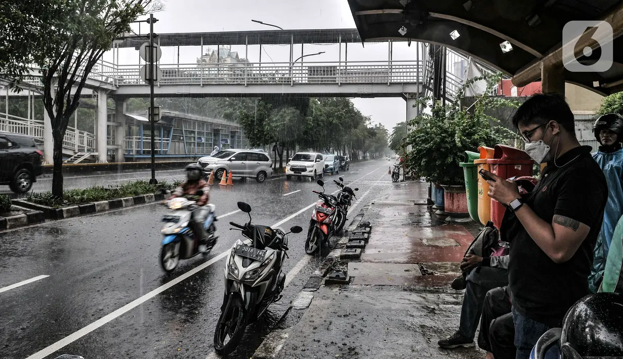 Pejalan kaki dan pengendara motor berteduh saat hujan di Jalan Pramuka, Jakarta, Kamis (18/2/2021). BMKG mengimbau pengguna jalan agar berhati-hati saat berkendara karena musim hujan disertai angin kencang diprediksi terus berlanjut hingga akhir Februari. (merdeka.com/Iqbal S Nugroho)