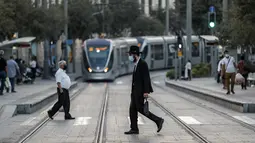 Seorang pria Yahudi Ortodoks, yang mengenakan masker karena pandemi virus corona COVID-19, melintasi jalan melewati Kereta Api Yerusalem di Yerusalem (26/10/2020). (AFP/Emmanuel Dunand)