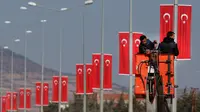 Buruh memasang bendera di tiang listrik menuju perbatasan Oncupinar di Kota Kilis, Turki, Senin (29/1). Bentrokan sempat meletus di puncak bukit strategis di Suriah karena milisi Kurdi mencoba mendapatkan kembali kontrol. (AP Photo/Lefteris Pitarakis)