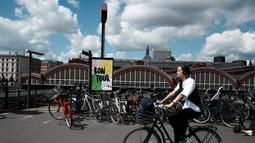 Seorang perempuan bersepeda melewati plakat bertuliskan "Enjoy the Tour" di Kopenhagen, Denmark, Selasa (28/6/2022), saat negara itu bersiap untuk menjadi tuan rumah tiga tahap pertama dari Tour de France Cycling Race mulai 1 Juli mendatang. (AP Photo/Thibault Camus)