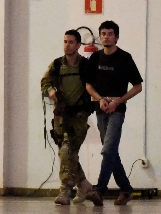 Terduga teroris berjalan dikawal oleh polisi di hanggar Polisi Federal Brasil di bandara di Brasil, (21/7). Kepolisan Brasil menangkap 10 orang amatiran yang disebut seakan-akan telah menyatakan kesetiannya kepada ISIS.( AFP PHOTO/Evaristo SA)