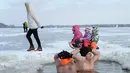 Anak-anak berkereta luncur melewati penggemar renang es di Danau Zalew Zegrzynski di Nieporet, Polandia, Minggu (25/2). Gelombang dingin sedang melanda Polandia. (AP Photo/Alik Keplicz)
