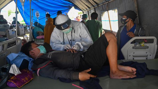 Seorang pria yang terluka dalam gempa dengan magnitudo 6,2 menerima perawatan di tempat penampungan sementara di luar Rumah Sakit Regional Sulbar, Mamuju, Sulawesi Barat, Minggu (17/1/2021). Mereka dirawat di dalam tenda darurat untuk mengantisipasi gempa susulan. (ADEK BERRY/AFP)