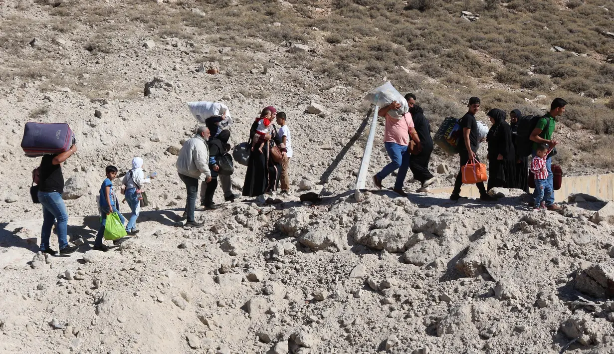 Orang-orang yang melarikan diri dari pengeboman Israel di Lebanon, berjalan di sekitar area lubang yang disebabkan oleh serangan Israel, di daerah Masnaa di sisi perbatasan Lebanon dengan Suriah, pada 4 Oktober 2024. (HASSAN JARRAH/AFP)