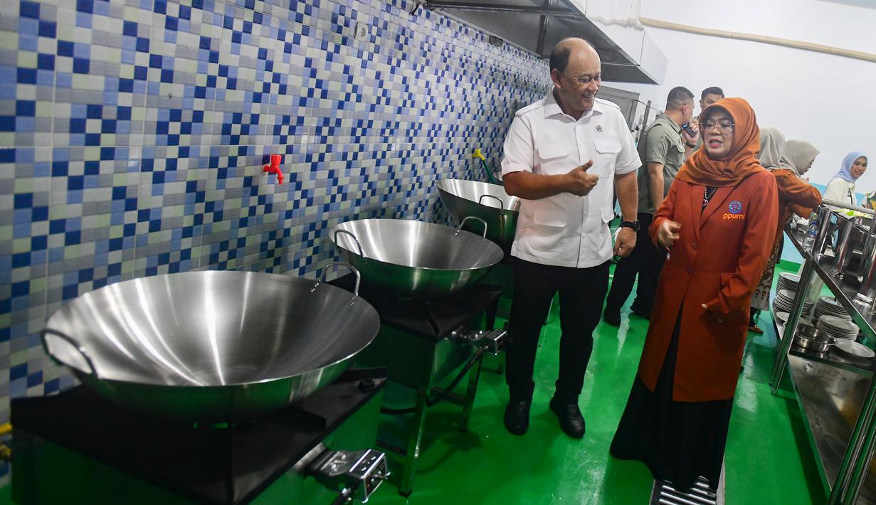 Selain aspek ekonomi, dapur SPPG Terintegrasi juga menempatkan perempuan sebagai aktor utama dalam pengelolaannya. PPUMI mendorong peran perempuan sebagai garda terdepan dengan komposisi relawan sebesar 70 persen perempuan dan 30 persen laki-laki. Pendekatan ini sejalan dengan semangat membangun ekonomi perempuan untuk meningkatkan kesejahteraan keluarga. Tampak dalam foto, Kepala Badan Gizi Nasional (BGN), Dadan Hindayana bersama Ketua Umum Pemberdayaan Perempuan UMKM Indonesia (PPUMI), Munifah Syarwani mengecek kondisi dapur Satuan Pelayanan Pemenuhan Gizi (SPPG) saat Grand Launching Nasional SPPG Terintegrasi di Lapangan Dapur SPPG-MBG kawasan Tanah Sareal Kota Bogor, Jawa Barat, Selasa (23/12/2025). (merdeka.com/Arie Basuki)